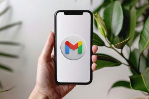 A person holding a smartphone displaying the Gmail logo in front of a plant, representing digital productivity and inbox organization