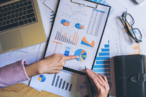 Hands pointing at marketing charts and graphs on a desk with a laptop and planner, illustrating seminar planning and data-driven results